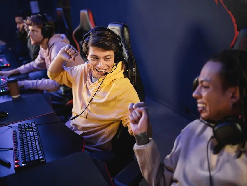 Esports-teamgenoten vieren samen hun overwinning met hun headsets op achter hun gaming-pc’s; ze glimlachen en geven elkaar een fist bump tijdens een multiplayer-wedstrijd